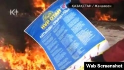 Жұмысшы киіміндегі адам президентшіл «Нұр Отан» партиясының плакатын отқа тастап жатыр. Жаңаөзен, 16 желтоқсан, 2011 ж. К+ телеарнасы бейнехабарынан алынған скриншот.